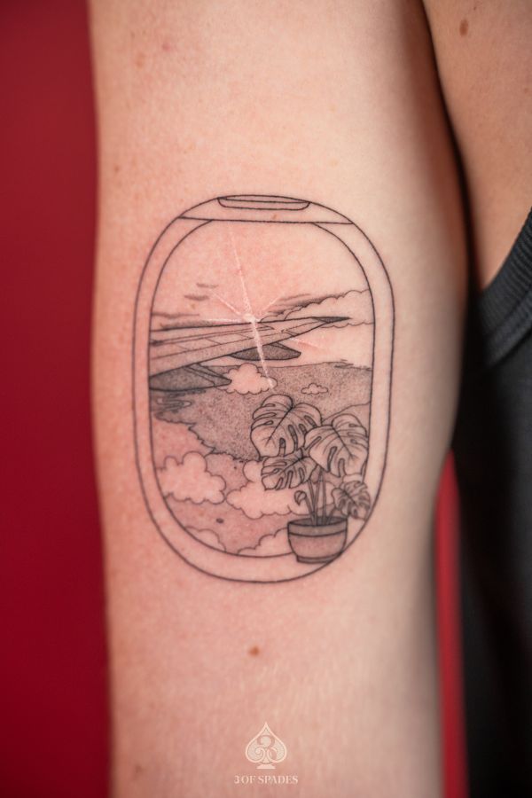 Fine line tattoo on upper arm showing a scenic view from an airplane window with mountains, clouds, and a potted plant – done at 3 Of Spades Tattoo Studio in Hanoi.