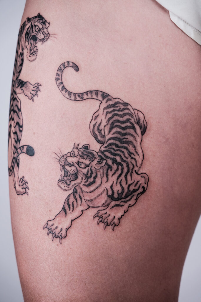 Crouching blackwork tiger tattoo on thigh, inked at a Hanoi tattoo studio with a focus on traditional Asian-inspired designs.