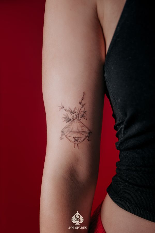 Fineline tattoo of a Vietnamese conical hat (nón lá) with flowers, symbolizing cultural beauty, tattooed in Hanoi.