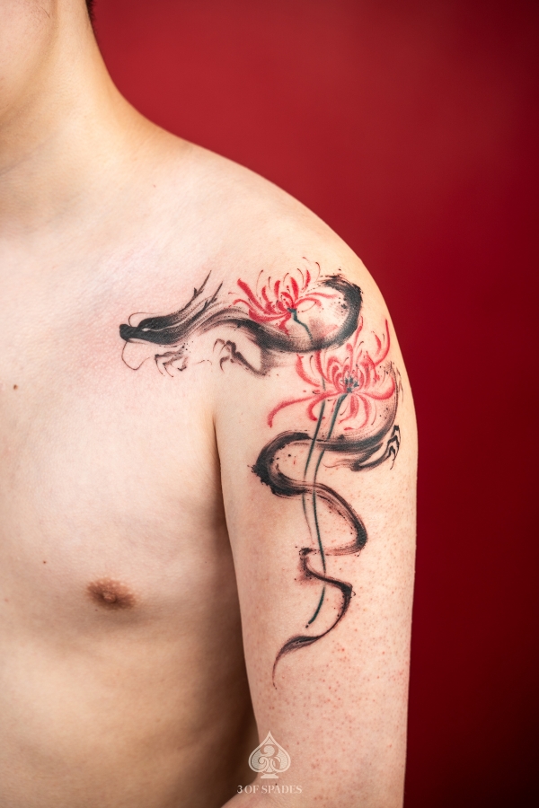 Abstract black dragon and red spider lily tattoo on upper arm and shoulder – custom Asian-inspired design at 3 Of Spades Tattoo Studio in Hanoi.