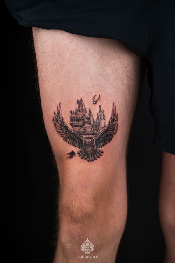 Black and grey Hogwarts castle tattoo with owl and flying snitch, done on thigh at a tattoo studio in Hanoi.