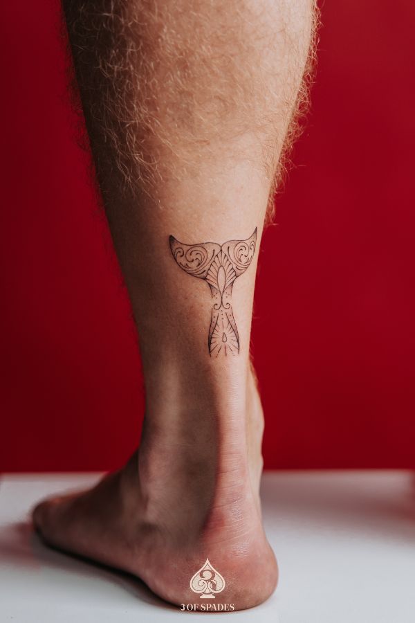 Minimal whale tail tattoo in ornamental linework style, placed on the lower leg, tattooed in Hanoi.
