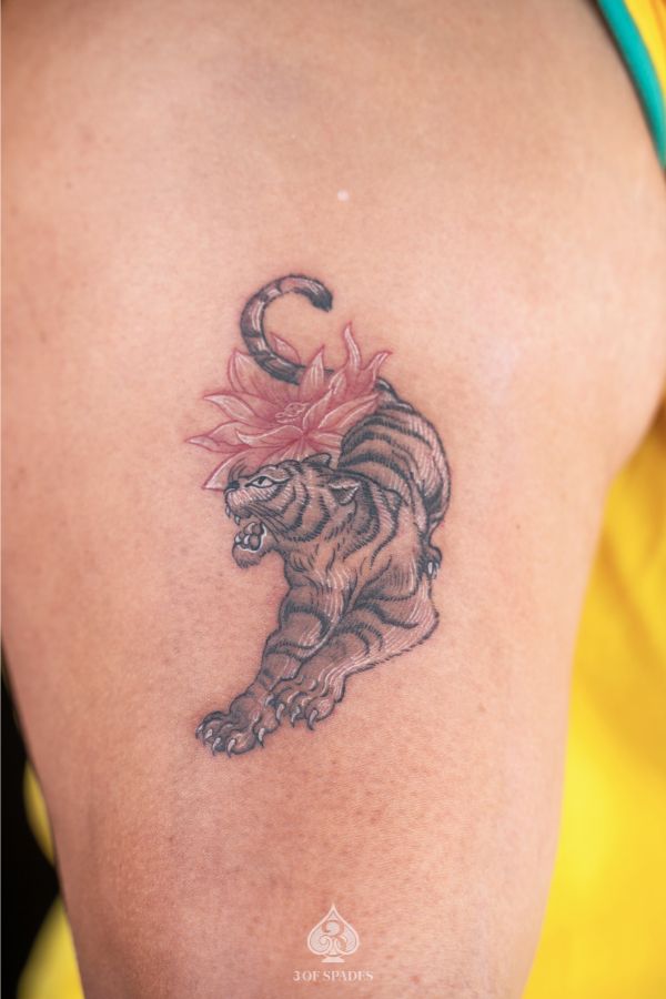 Traditional tiger tattoo with pink lotus flower on upper arm, symbolizing strength and inner peace.
