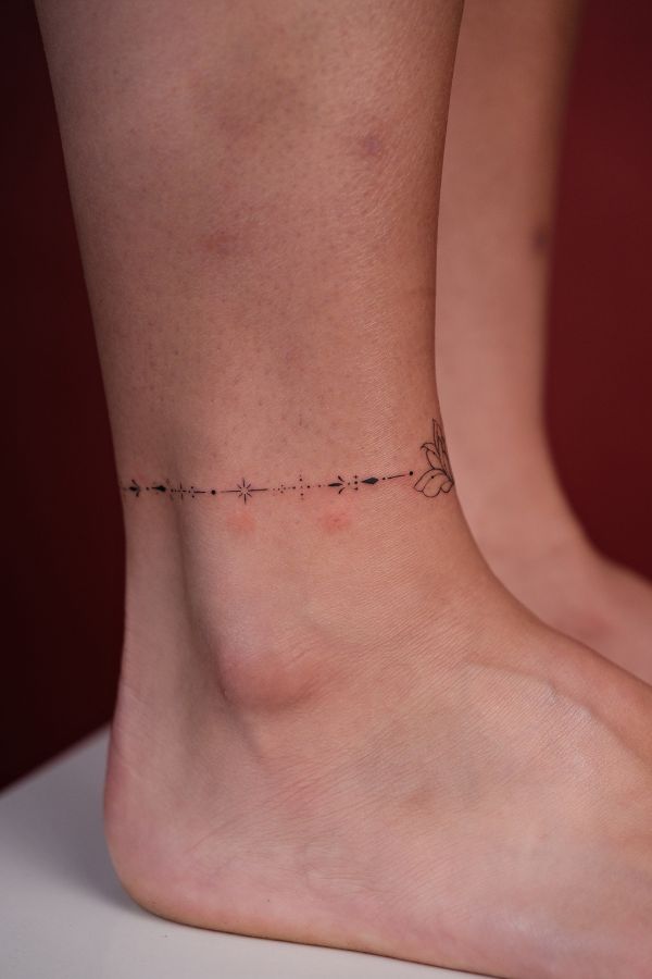 Minimalist ankle band tattoo with fine line floral and star elements – tattoo Hanoi
