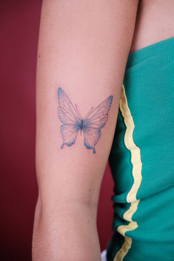 Blue butterfly tattoo on forearm in fine line style – custom tattoo Hanoi at 3 of Spades studio.