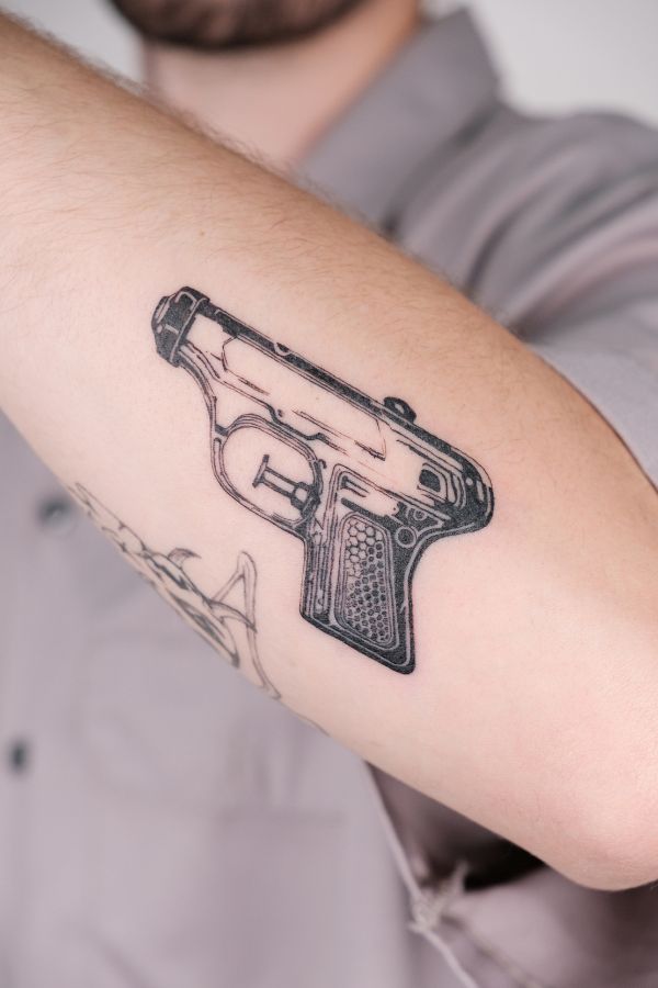 Blackwork gun tattoo on arm with technical linework and dotwork detailing, tattooed at 3 Of Spades Hanoi.