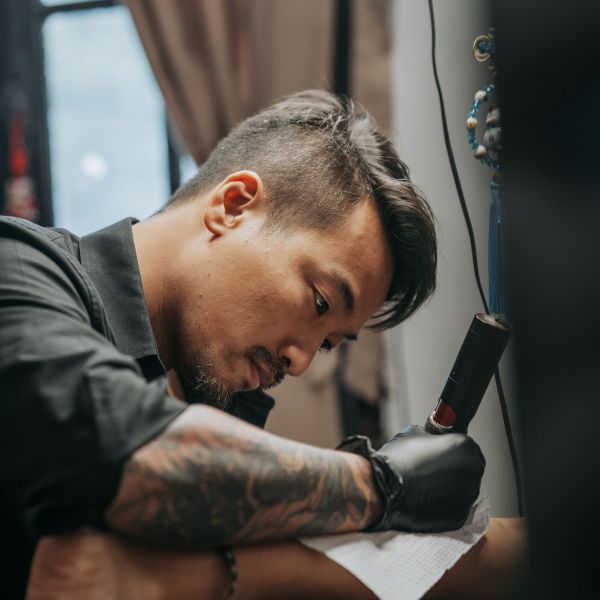 Tattoo artist at 3 Of Spades in Hanoi focused while tattooing a client.