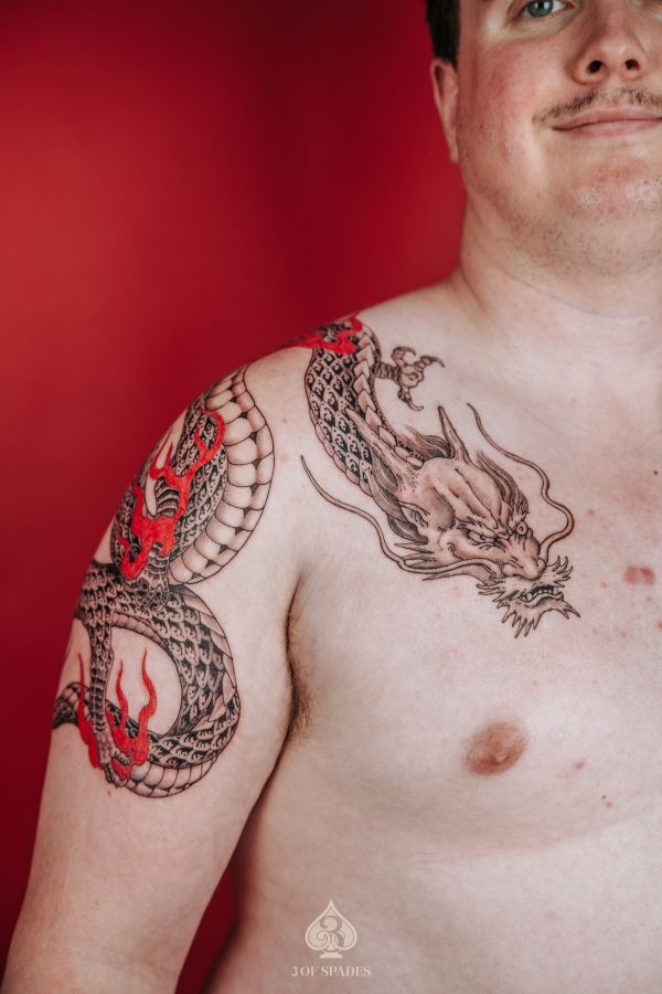 Black and red oriental dragon tattoo on shoulder and chest by artist at 3 Of Spades Tattoo Hanoi