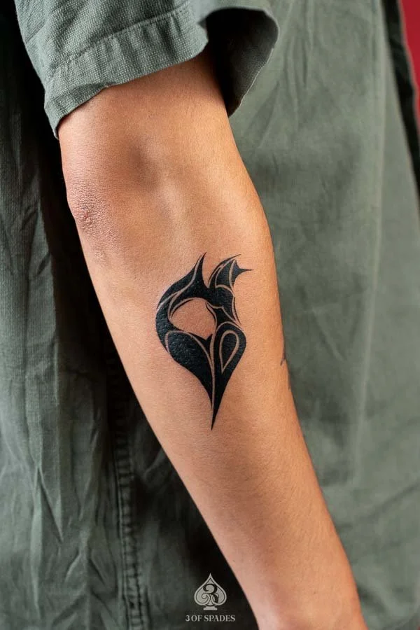 Blackwork Heart Logo Tattoo featuring a bold abstract heart symbol with sharp curves and solid black ink on the forearm at 3 of Spades Hanoi Tattoo.