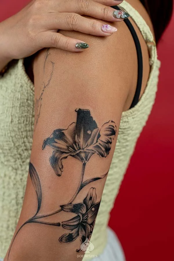 Modern Blackwork Tattoo: Blackwork Lily Back Arm Tattoo featuring elegant lily petals, detailed botanical linework, and black ink floral artwork on the back of the upper arm at 3 of Spades Hanoi Tattoo.