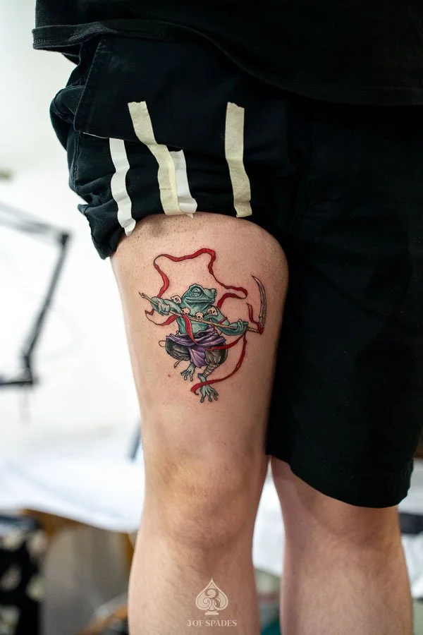 Color Frog Thigh Tattoo concept featuring a colorful frog with expressive eyes, vibrant amphibian markings, and detailed artistic shading at 3 of Spades Hanoi Tattoo.