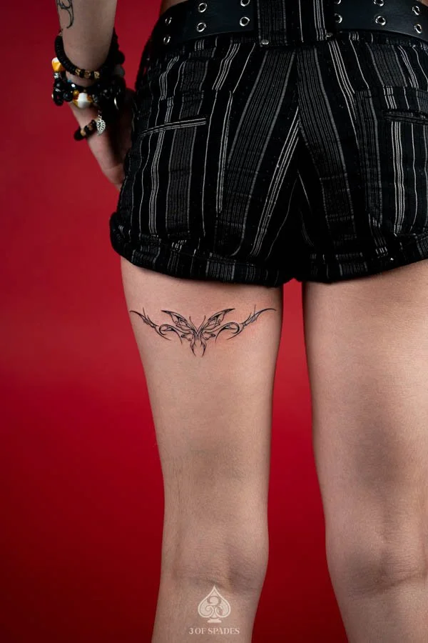 Sigilism Butterfly Hamstrings Tattoo featuring symmetrical abstract butterfly wings, sharp blackwork lines, and cyber sigilism inspired ornamental details on the back of the thigh at 3 of Spades Hanoi Tattoo.