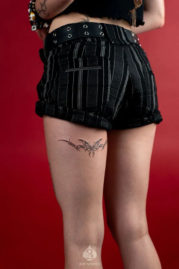 Sigilism Butterfly Hamstrings Tattoo featuring symmetrical abstract butterfly wings, sharp blackwork lines, and cyber sigilism inspired ornamental details on the back of the thigh at 3 of Spades Hanoi Tattoo.
