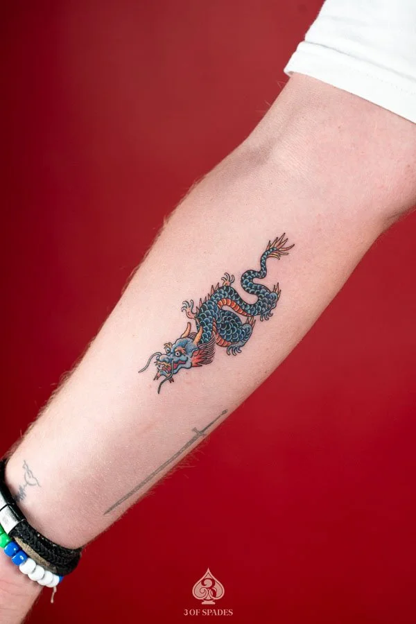 A colorful small oldschool dragon tattoo featuring a coiled blue dragon, vibrant orange accents, and bold traditional linework.