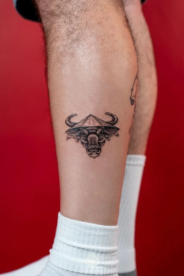 Vietnam Inspired Water Buffalo Tattoo on the leg featuring a detailed black and grey buffalo portrait with curved horns, expressive eyes, and a traditional Vietnamese nón lá conical hat by 3 of Spades Hanoi Tattoo.