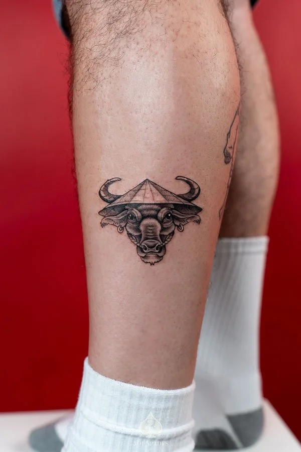 Vietnam Inspired Water Buffalo Tattoo on the leg featuring a detailed black and grey buffalo portrait with curved horns, expressive eyes, and a traditional Vietnamese nón lá conical hat by 3 of Spades Hanoi Tattoo.