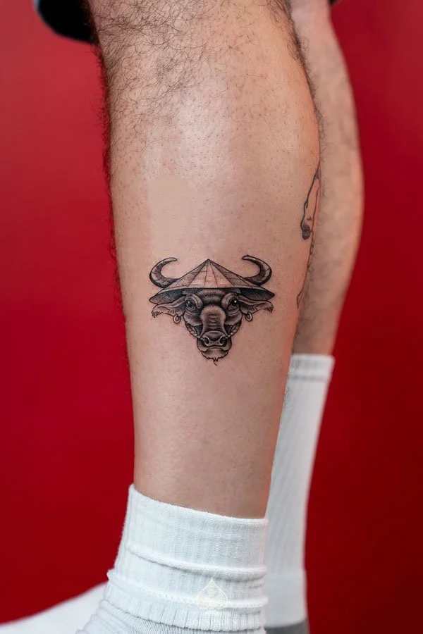 Vietnam Inspired Water Buffalo Tattoo on the leg featuring a detailed black and grey buffalo portrait with curved horns, expressive eyes, and a traditional Vietnamese nón lá conical hat by 3 of Spades Hanoi Tattoo.